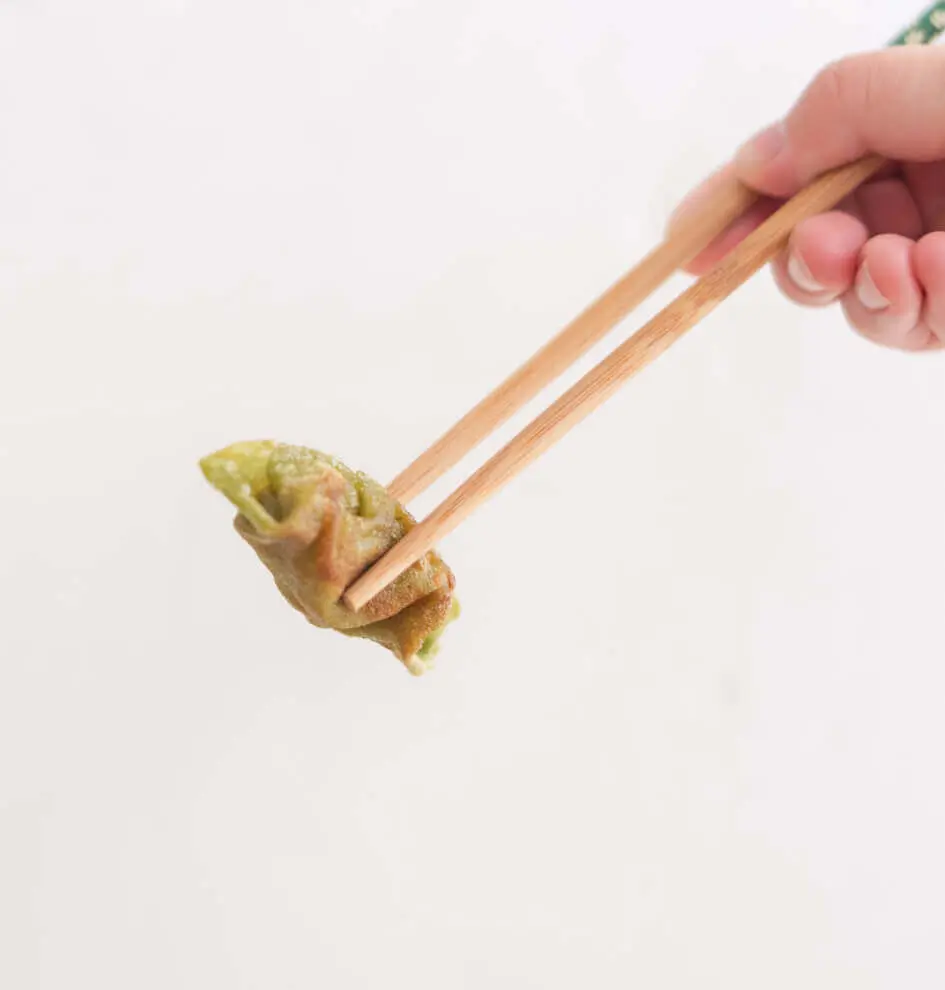 a human hand use chopsticks to pick up a dumpling