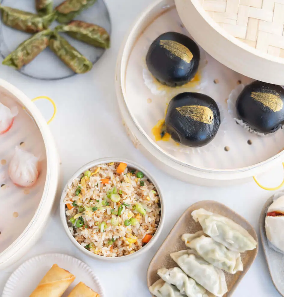 3 black buns, a bowl of fried rice, and a plate of dumplings